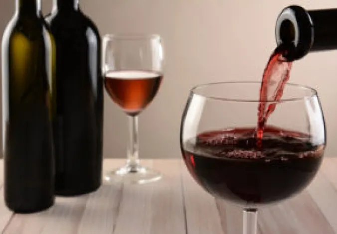 Closeup of a glass of wine and a bottle pouring. Out of focus wine bottles and another wineglass are in the background. Horizontal still life with warm tones and light to dark background lighting.