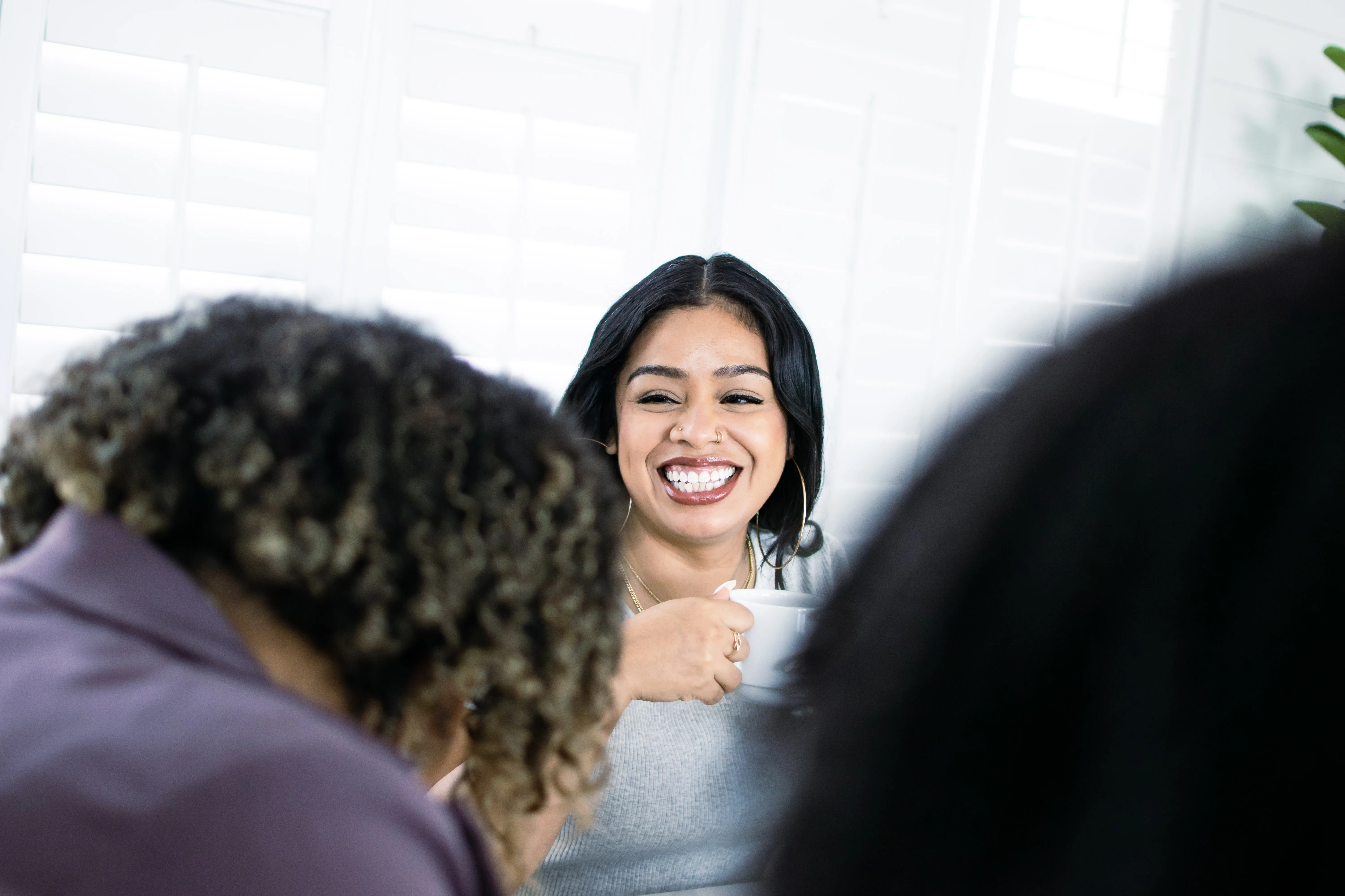 Latina woman laughs with colleagues while holding a white cup coffee mug