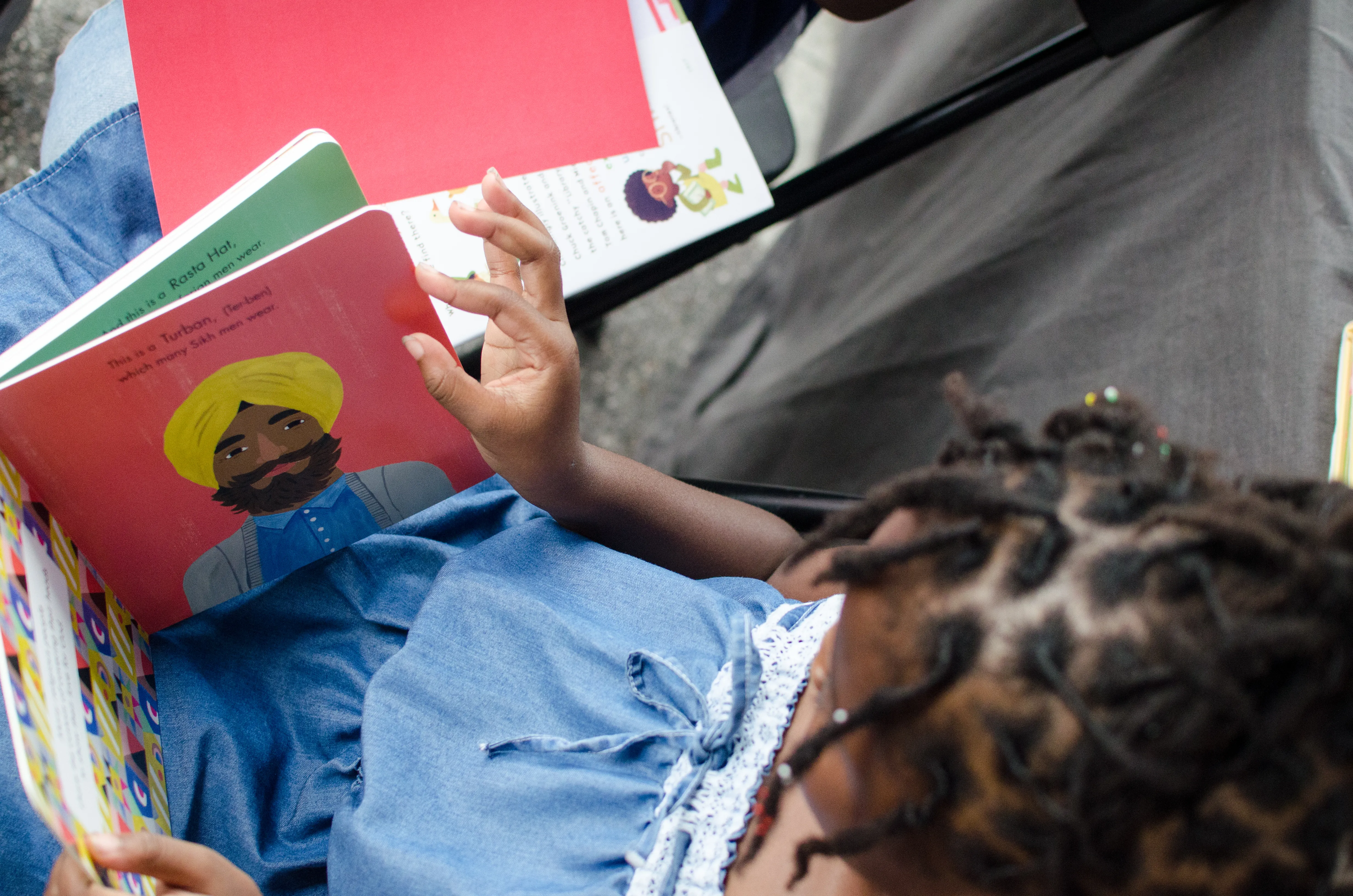 Black child reading board book with pictures depicting head dressings.
