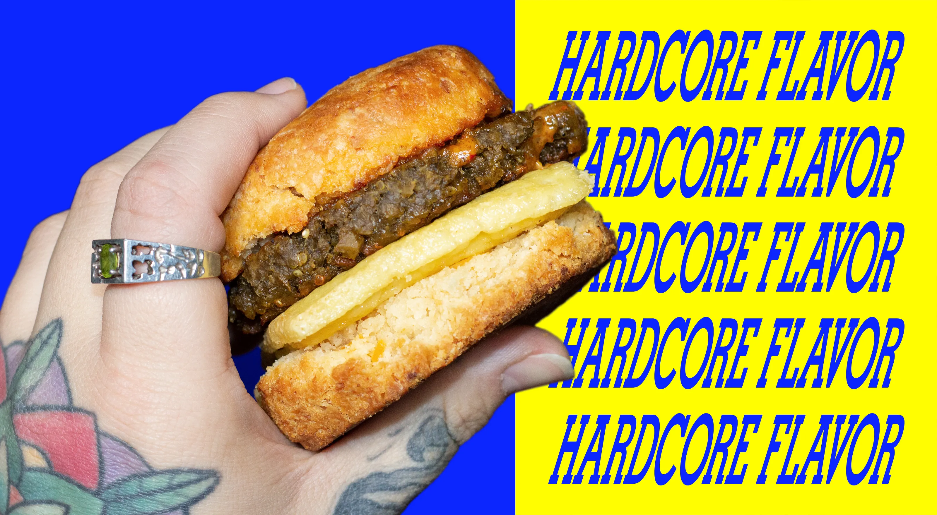 Split rectangular image. Left side features a tattooed hand with a ring holding a bizkit breakfast sandwich with vegan egg, sausage and sauce on a blue background. The right side features a yellow background with the word "hardcore" written five times in blue.