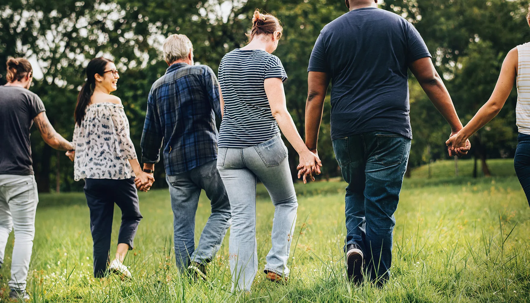 Group of adults walking hand-in-hand in a field.