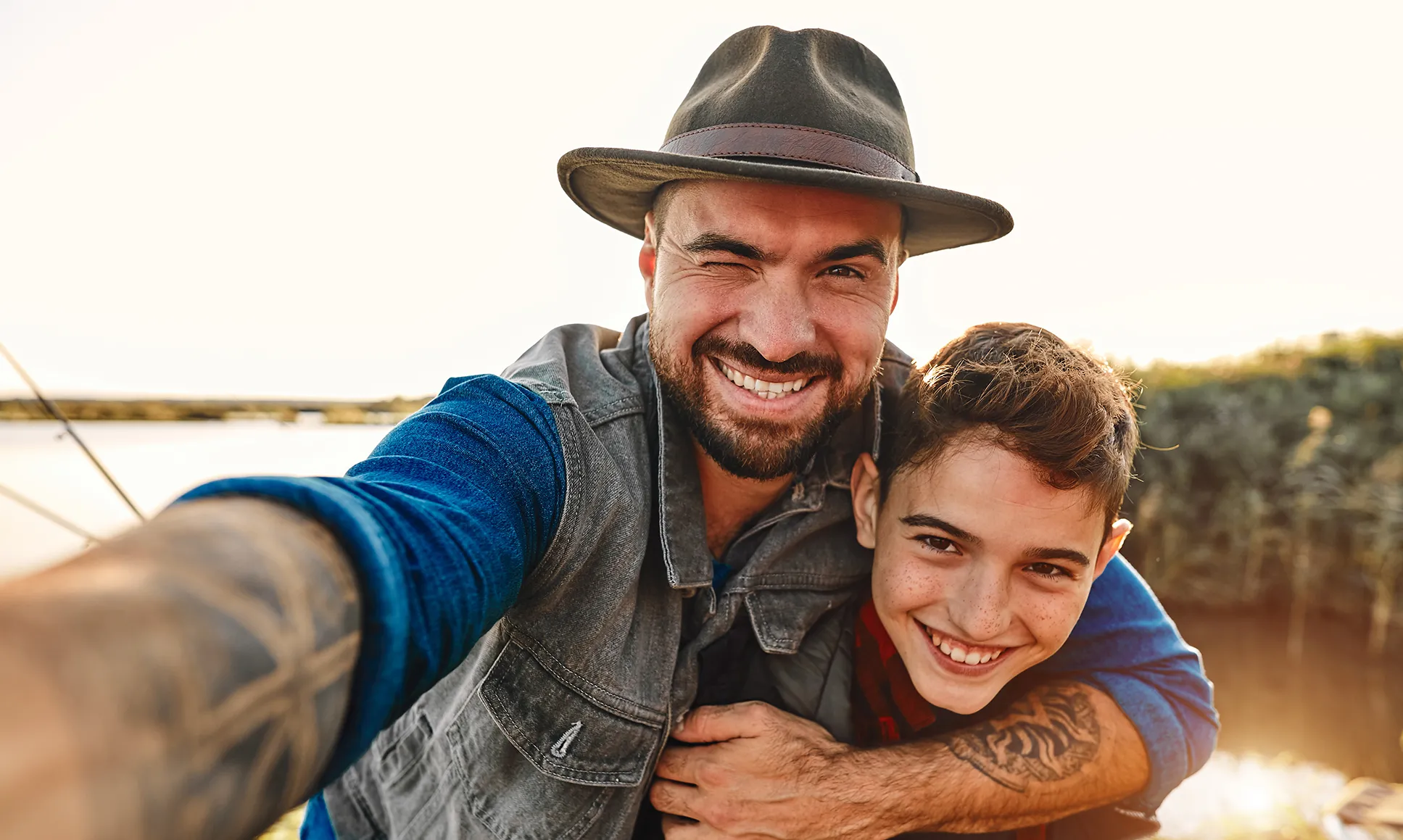 Father hugging son, both smiling, with a lake behind them.