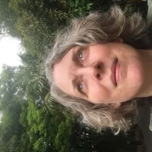 Blonde hair woman looking up with green trees in the background